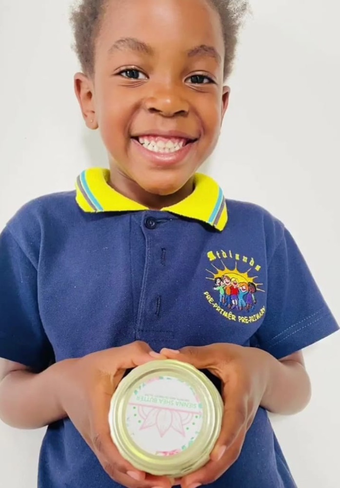 A smiling child holding a tub of Sienna Shea Butter